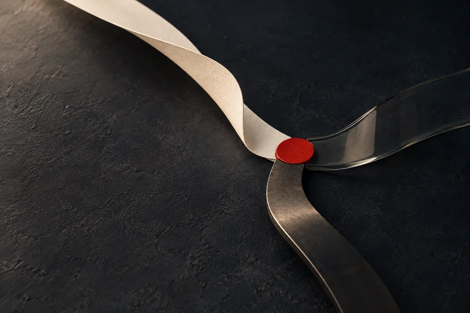 Una cinta de papel y otra de vidrio se cruzan, sujetas por un sello rojo.